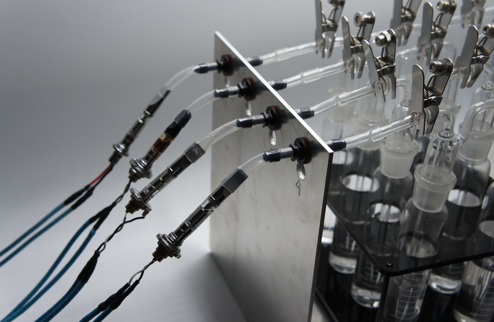 Four identical vape cartridges mounted on a 4-channel UVM, each connected by its own 510 power cable and feeding a separate glass impinger through the front bulkhead ports