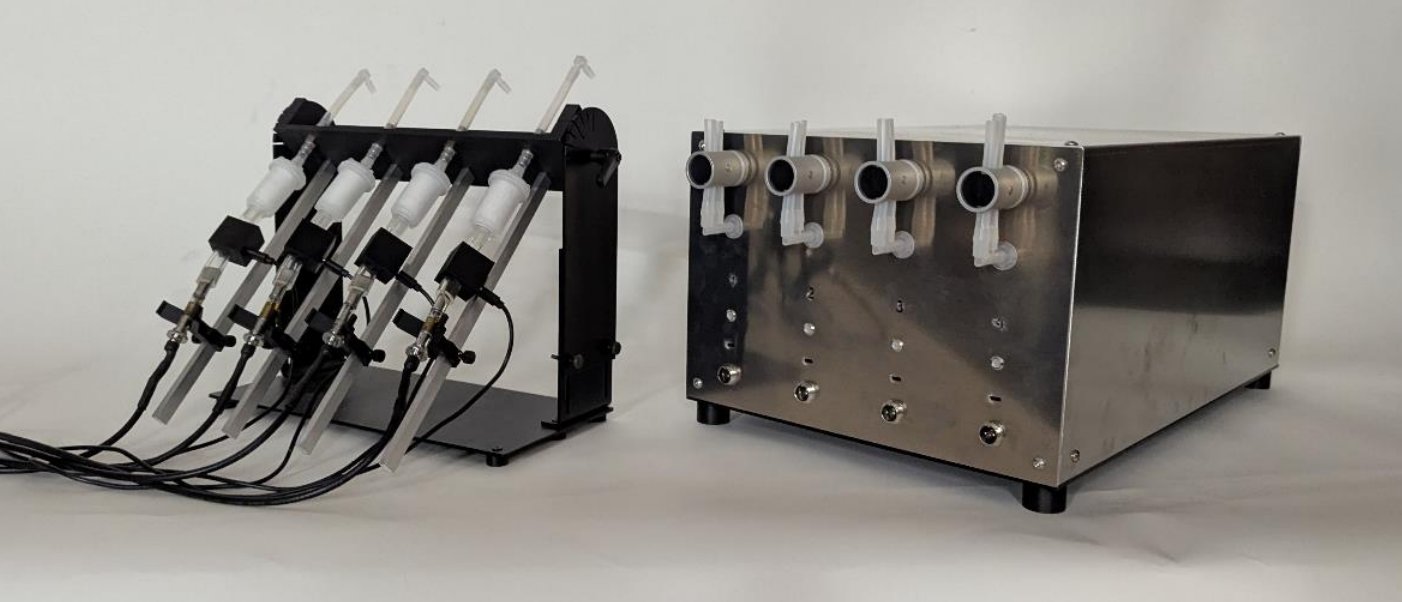 Gram four-channel Universal Vaping Machine — stainless-steel four-channel electronics enclosure beside the black sample-mounting rack with filter holders and 510 power cables